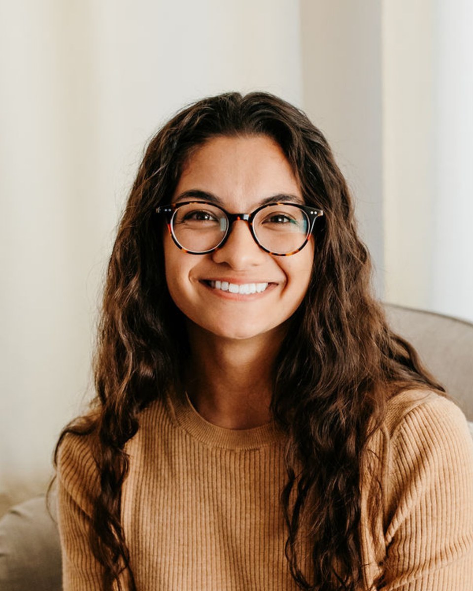 Leina Gilster, smiling, in a tan sweater and round glasses